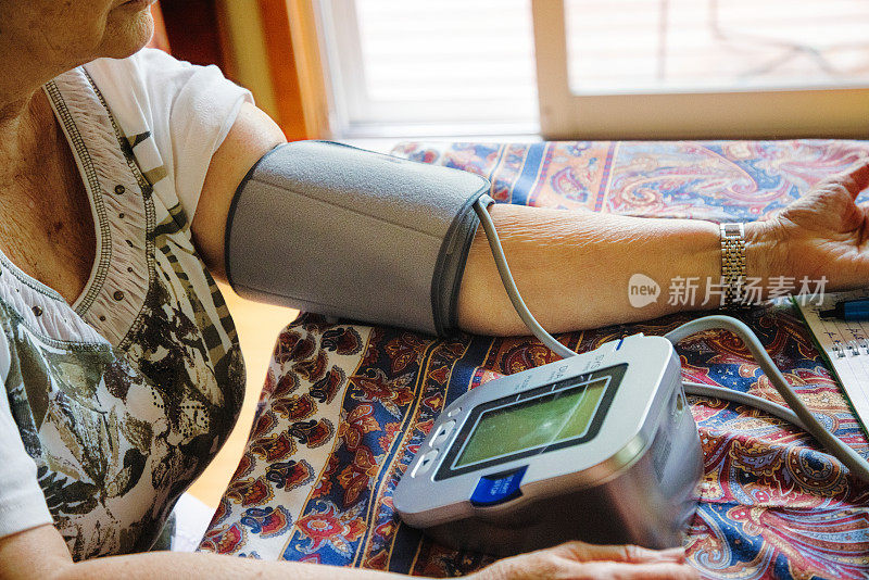 图为一位老年妇女在家中用监控设备测量血压时手臂上的特写镜头