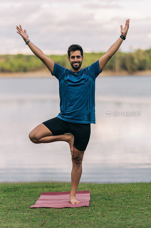 一个微笑的男子单腿站立在湖边做瑜伽