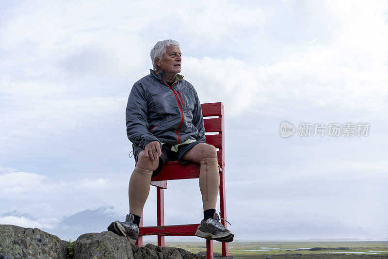 老人坐在巨大的红色椅子上，看着冰岛东南角的蝙蝠侠山