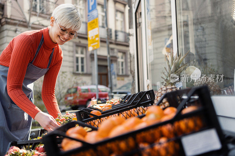 一个快乐的年轻女售货员在她的商店外面摆放水果的肖像