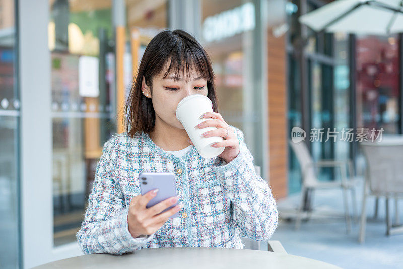 亚洲年轻女子在城市街道的咖啡店里使用智能手机