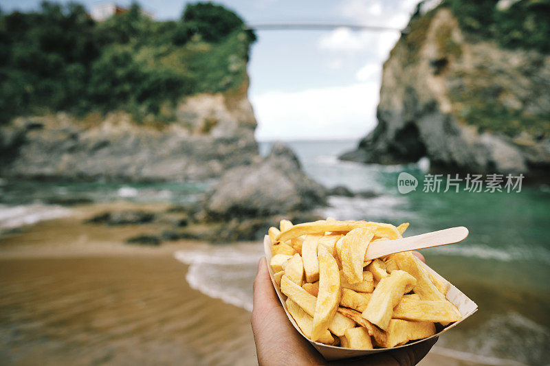 6月一个阳光明媚的日子，在康沃尔郡纽基镇海滩，一只手拿着一盒薯片。