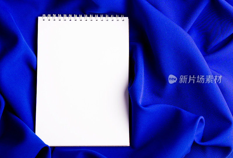 把笔记本的空白页放在蓝色布料的折痕上