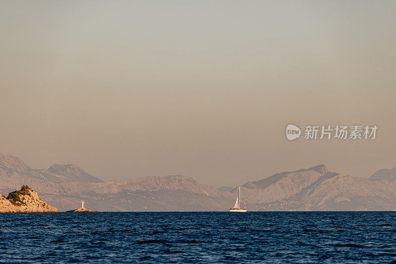 帆船在远处的一个岩石岛前面有很多山，灯塔旁边的船，从海上看