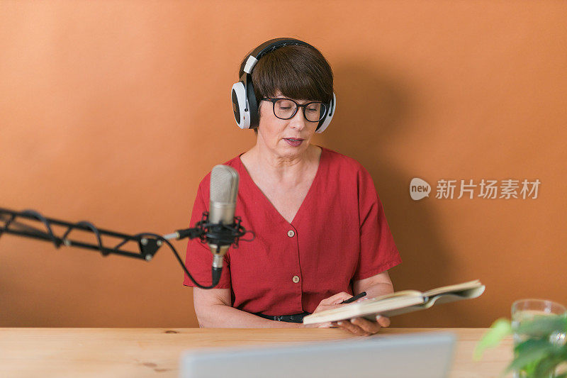 中年女性电台主持人对着麦克风边讲边读新闻——电台在线播报概念