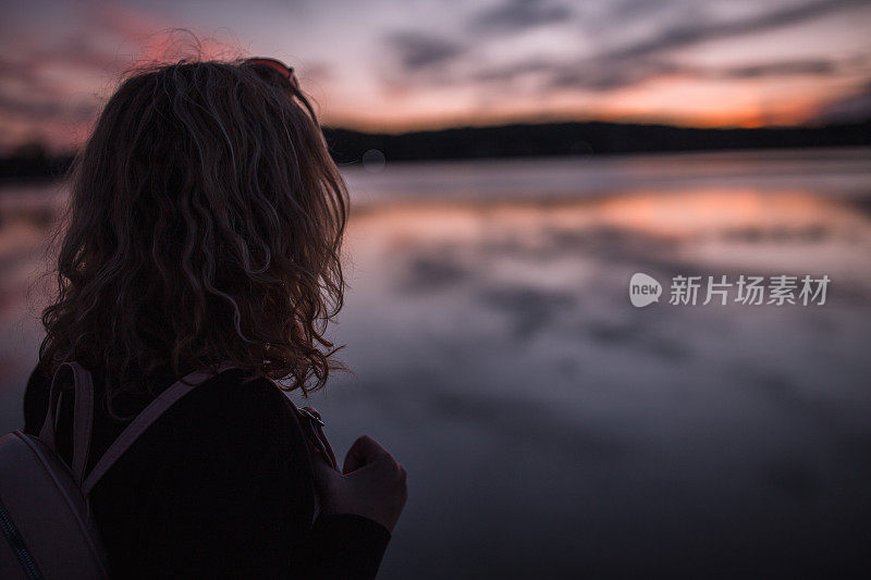 一头浓密头发的面目全非的女子在湖上欣赏日落