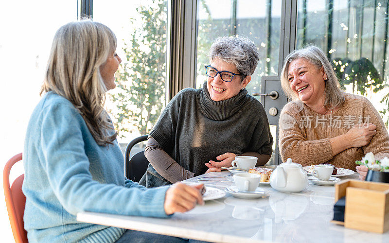 一群老年妇女在自助餐厅吃早餐，三位退休的女性朋友正在喝着茶和咖啡，吃着巧克力蛋糕庆祝周年纪念日