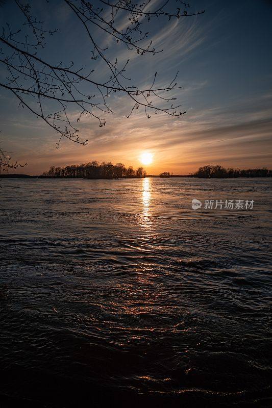 夏天的日落时分，湖水被树木环绕，太阳在水面上的倒影
