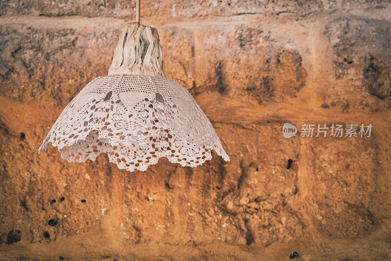 一个覆盖着花边的老式装饰灯站在一个摇摇欲坠的石墙背景前。