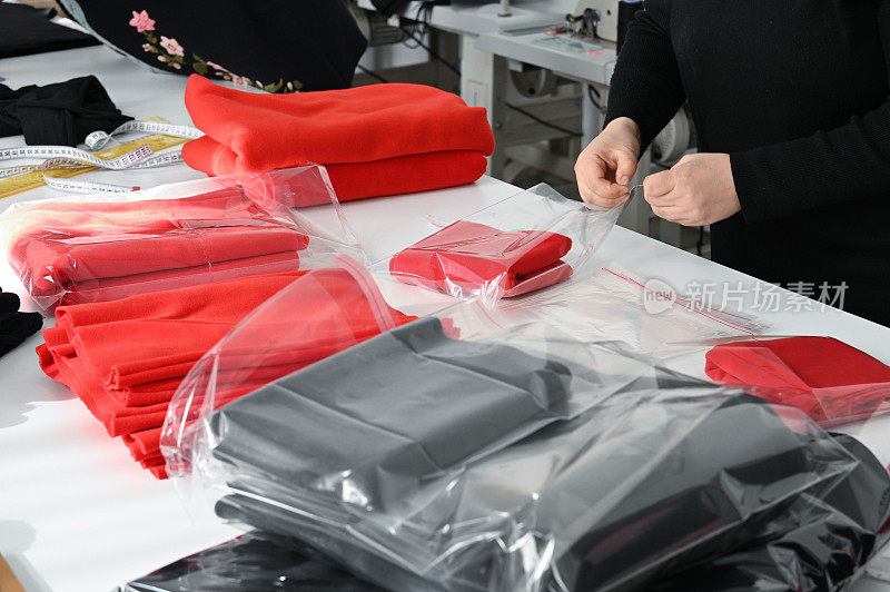 妇女包装红色和黑色羊毛织物与透明袋在白色柜台。