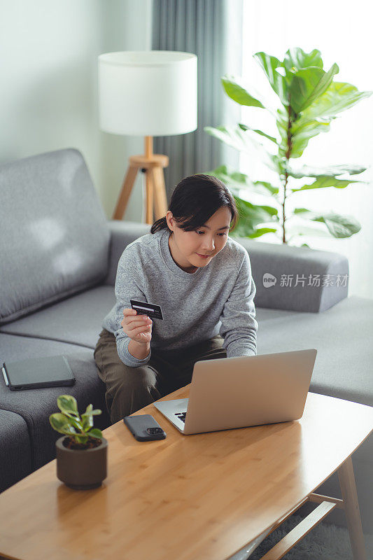 亚洲女性喜欢坐在家里的客厅里用笔记本电脑和信用卡在线支付。