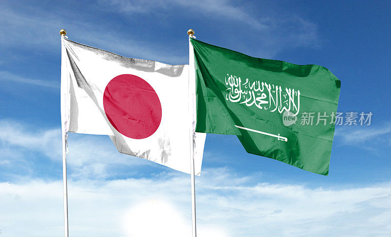 多云天空上的日本国旗和沙特阿拉伯国旗。在天空中摇曳