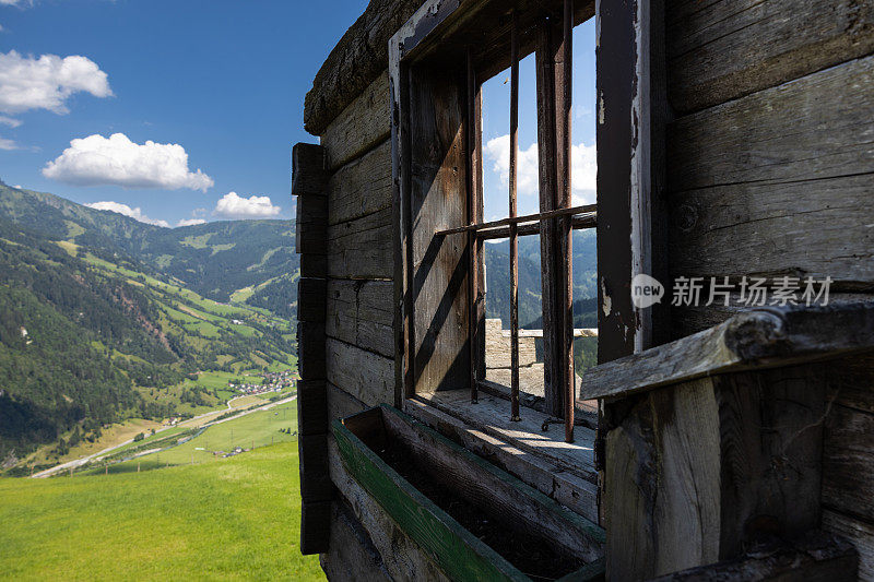 一堵带窗户的墙，从一座老房子里保留下来，背景是夏季的山景，奥地利