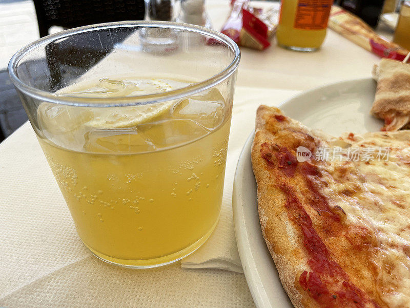 白色的盘子里有玛格丽特披萨，还有一杯柠檬片和冰块的碳酸橙饮料，餐厅场景的背景，焦点在前景
