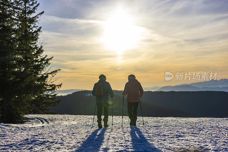 老夫妇手持登山杖在雪景上行走的后景