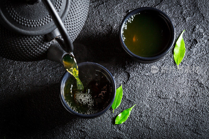 美味的绿茶配茶壶和茶杯放在黑岩上