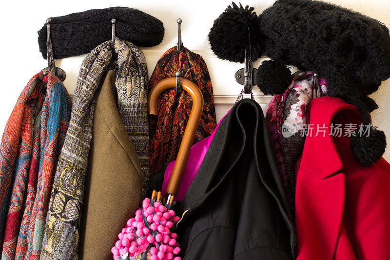 色彩鲜艳的衣服、大衣、帽子和伞挂在大衣钩上，冬天很冷