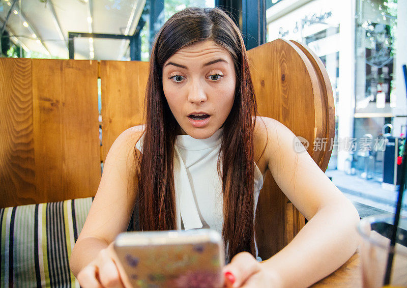 咖啡馆里拿着手机的惊讶女人