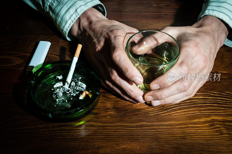 手握酒精饮料的男人与吸烟烟灰缸酒精饮料。