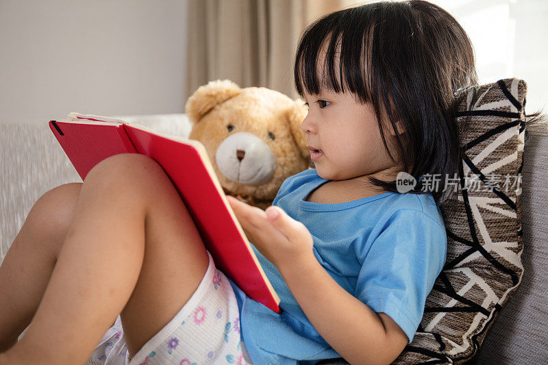 亚洲华人小女孩和泰迪熊一起看书