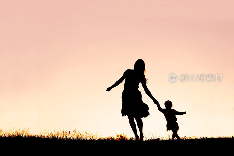 母亲和婴儿女儿在夕阳下奔跑和跳舞的剪影