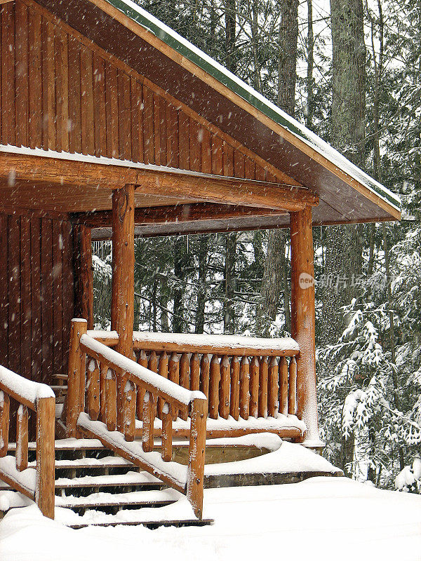 白雪覆盖的原木小屋门廊在树林