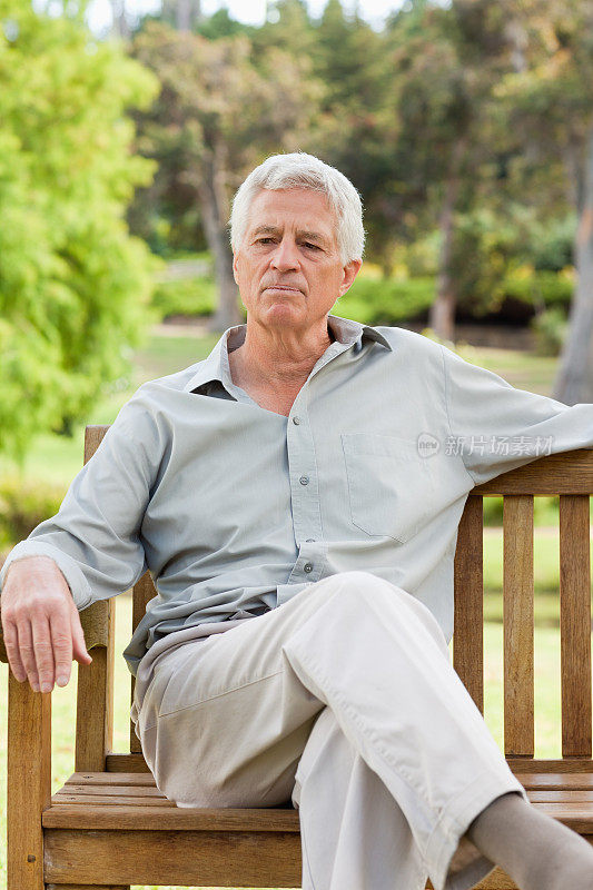 老人双腿交叉坐在公园长椅上思考