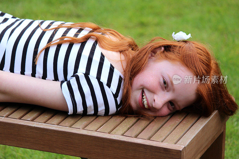 女孩躺在花园草坪上的木凳上