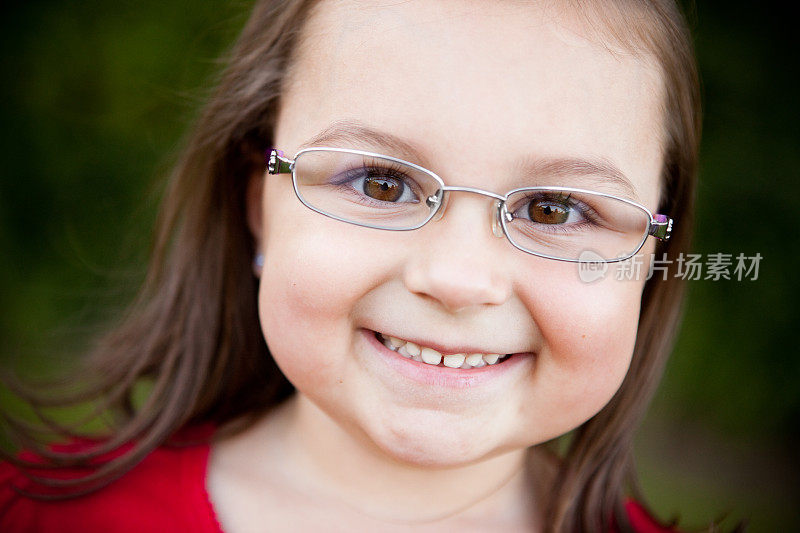 戴眼镜的快乐年轻女孩在外面微笑