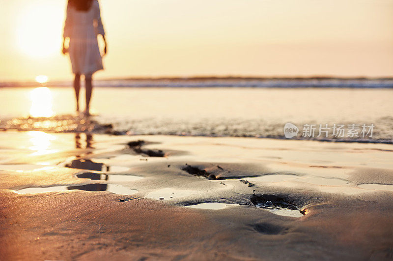 沙滩上有脚印，有个女人在阳光下走在后面