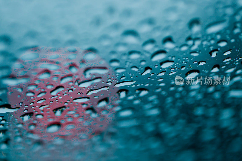 雨点落在挡风玻璃上，车头灯在背景中