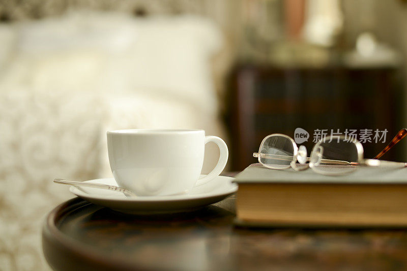 床边放着咖啡和书，戴着老花镜