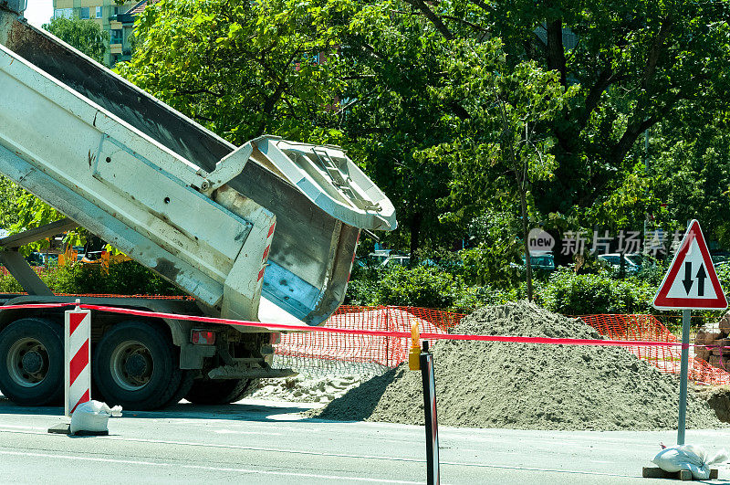 自卸卡车在街道工地上卸沙子。卡车的尾部。