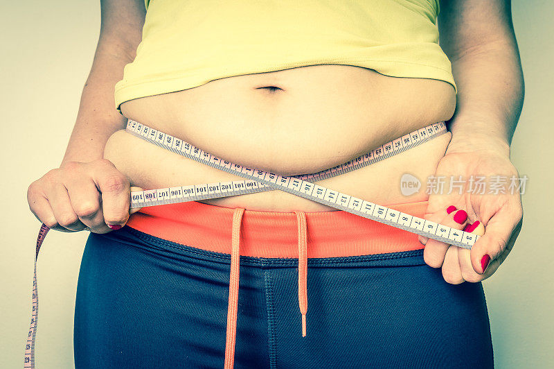 超重妇女用卷尺量肚子上的脂肪