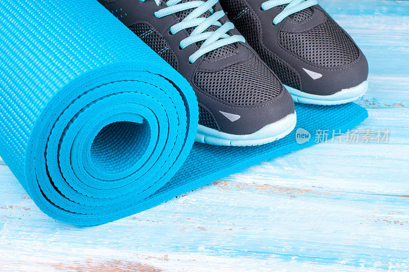 运动器材和运动鞋。瑜伽垫和运动鞋上的蓝色木制背景。健康的生活方式，健康的食品，运动和饮食的概念。本空间