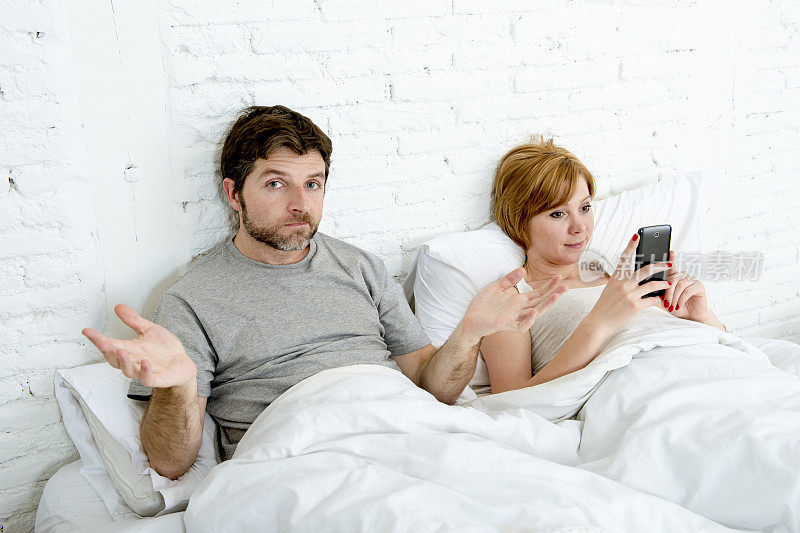 夫妻在床上丈夫沮丧的妻子使用手机