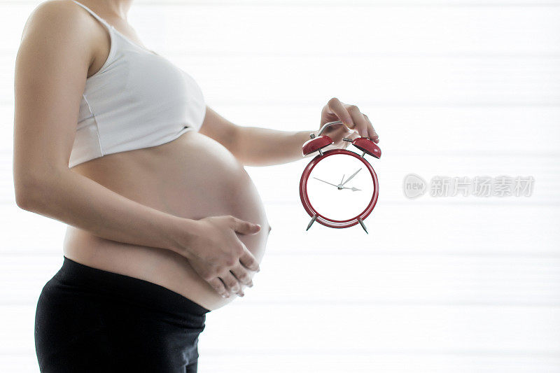 怀孕的肚子和妈妈手里滴答作响的时钟