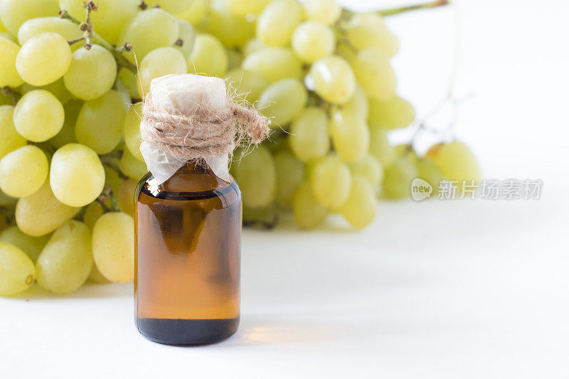 治疗葡萄籽油在一个玻璃缸，新鲜的葡萄在白色的背景，种子提取物具有抗氧化和滋养皮肤，水疗概念，选择性聚焦宏观前视图。生物、生态产品。