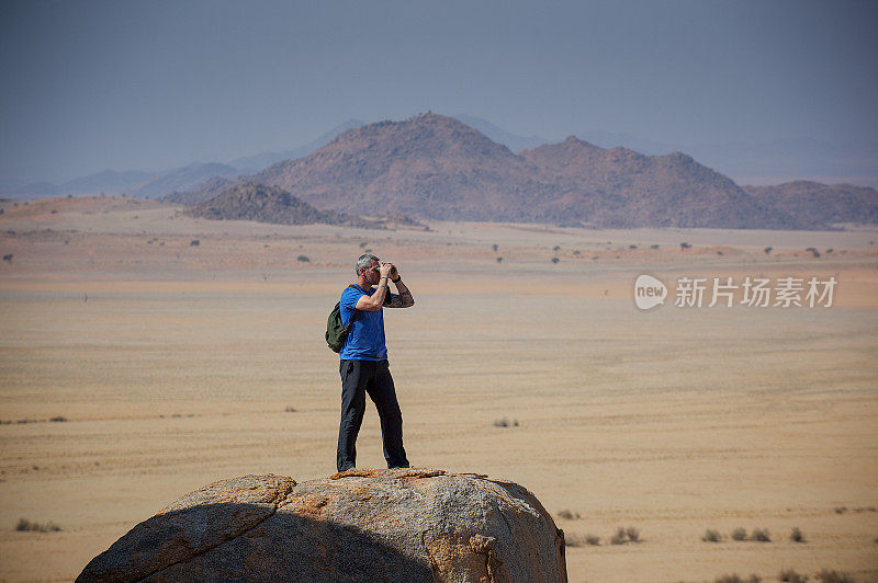 一个人拿着双筒望远镜站在沙漠的岩石上