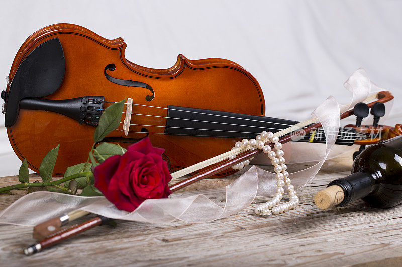 小提琴，红玫瑰，珍珠项链和酒在木桌上