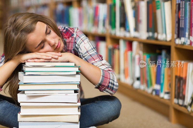 睡觉的学生坐在图书馆的地板上倚着一堆书