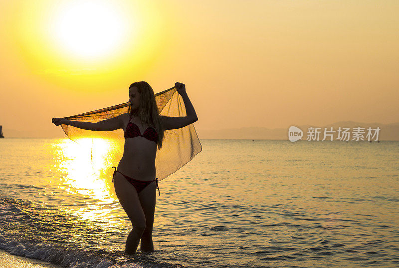 欢呼的女人在阳光下在海滩上张开双臂
