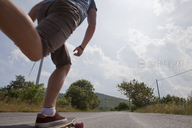 在意大利利古里亚的公路上，一个十几岁的男孩滑着滑板经过风力涡轮机