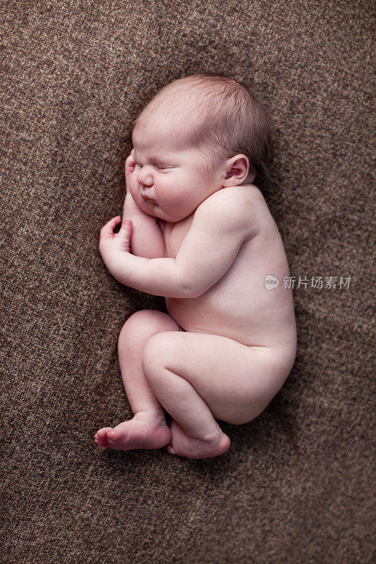 新生婴儿安静地睡在棕色毯子上的彩色图像