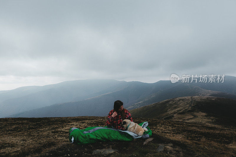 睡袋里的女人和狗在山中醒来