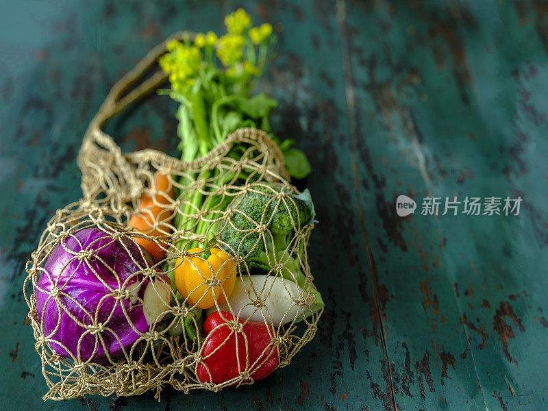 市场新鲜蔬菜在一个可重复使用的漂亮的网袋，在一个旧的绿松石色木桌子的背景。