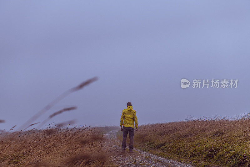 一个人站在海边的小路上，在一个秋日的海雾中。