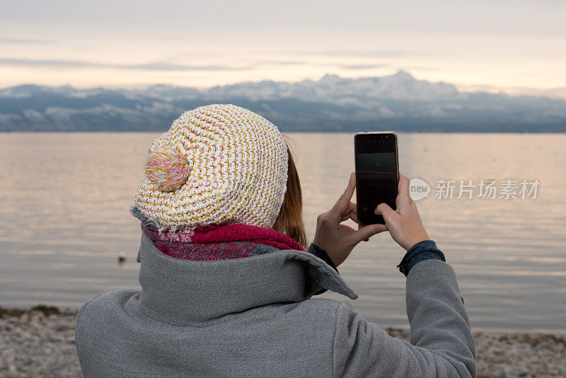 在康斯坦斯湖的冬天，女人用智能手机的肖像模式拍摄雪山Säntis