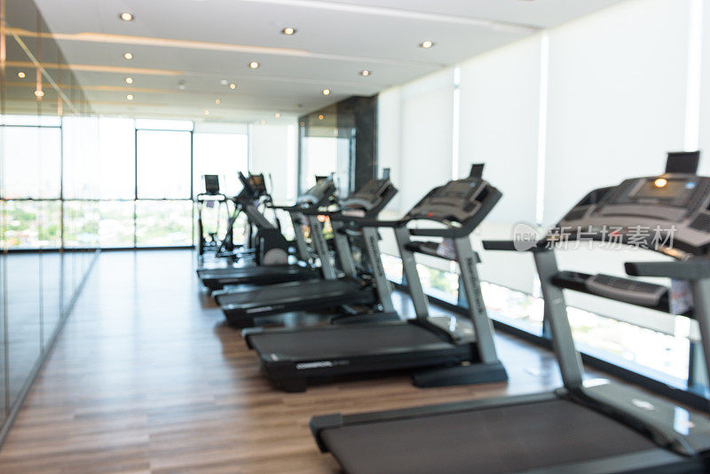 背景抽象模糊:健身房内部配备电动跑步机和设备。