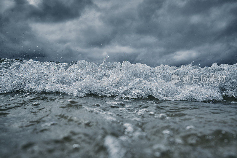 破碎的波浪接近相机在海面上与一个黑暗戏剧性的暴风雨天空。